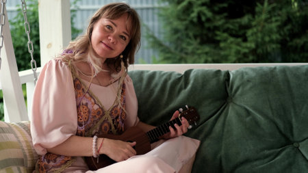 A woman in an elegant boho style dress plays the ukulele.の写真素材