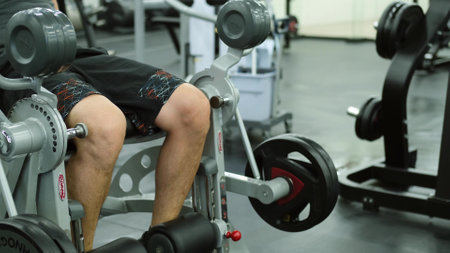Muscular man training in the gym, shaking the muscles of the legs with the help of an exercise...