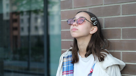 Portrait of a beautiful sad teenager girl on the street. Sad girl on the background of a brick wall