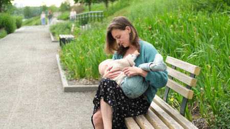 Mother breastfeeding her baby on a park bench on a summer dayの写真素材