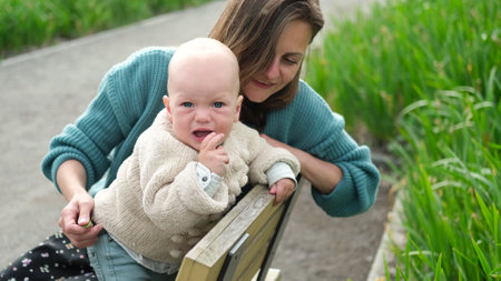Young mother with her cute baby on bench in parkの写真素材
