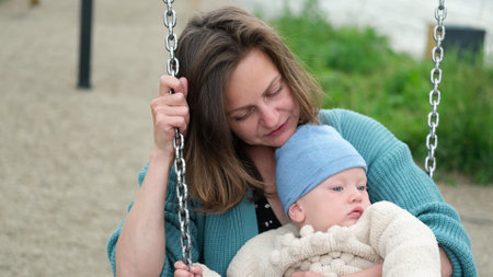 A young mother and a small child are swinging on a swing. Open. Childrens Day concept.