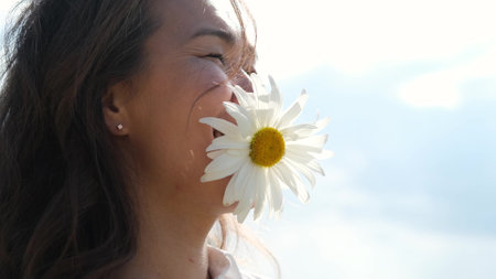 Happy woman with big chamomile in her mouth. A carefree girl enjoys freedom and tranquility in the countryside while on vacation. The concept of rest or relaxation and happiness or summer.の写真素材