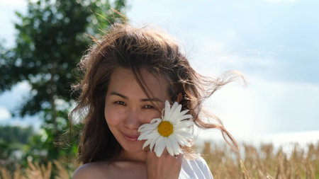 Happy woman with big chamomile in her hand in summer field. Carefree girl enjoys freedom and tranquility in the countryside during her vacation. The concept of rest or relaxation and happiness or summer.の写真素材