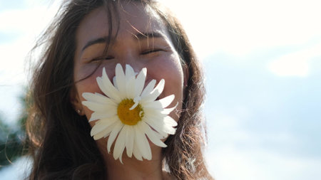 Happy woman with big chamomile in her mouth. A carefree girl enjoys freedom and tranquility in the countryside while on vacation. The concept of rest or relaxation and happiness or summer.の写真素材