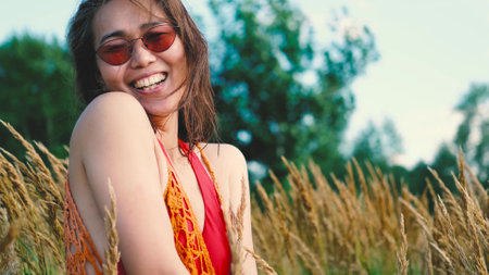 Happy free asian woman walking in tall grass on a sunny summer day. Portrait of a hippie woman in a bright orange boho style topの写真素材