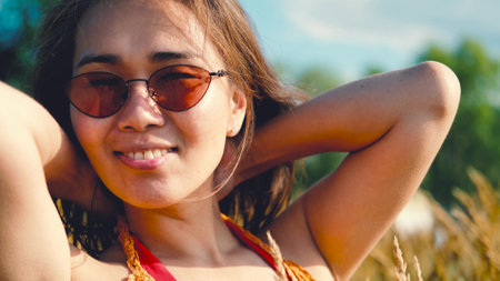 Happy free asian woman walking in tall grass on a sunny summer day. Portrait of a hippie woman in a bright orange boho style topの写真素材