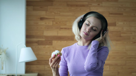 Beautiful sad girl spends time alone at home. The girl listens to music in headphones and eats sweet...