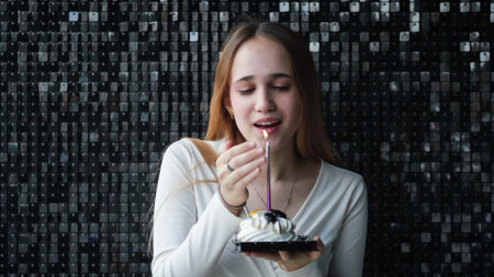 Cute teen girl blowing a candle in a festive little cake on a black shiny backgroundの写真素材