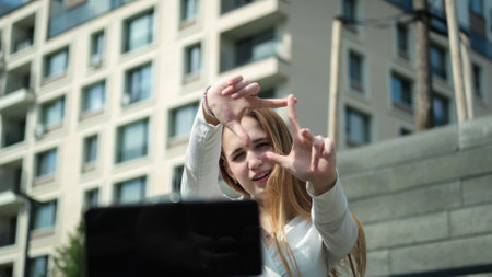 A cute teenage girl with long hair in a fashionable outfit maintains her personal blog, shoots a video on a smartphone outdoorsの写真素材