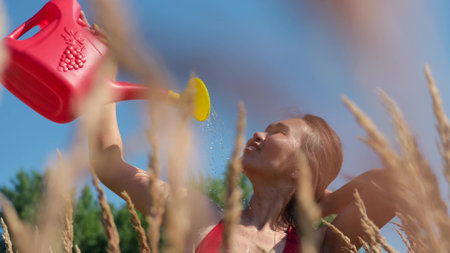 A young woman stands among a field with dry grass on a hot summer day. A woman pours water from a...