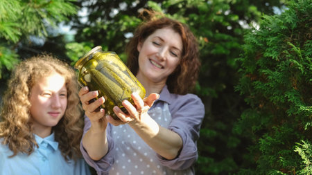 Mom and daughter prepare canned vegetables for the winter. On a warm autumn day, the family is doing household chores, picking vegetables for the winter. A woman and her teenage daughter show a jar of homemade pickled cucumbers. village foodの写真素材