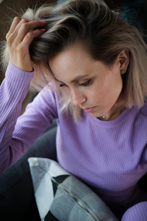 Beautiful blonde woman with purple house suit looks relaxed at homeの写真素材