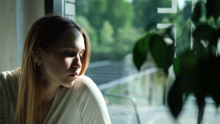 Sad young girl, teenager sitting at a cafe table in the rays of the bright summer sun