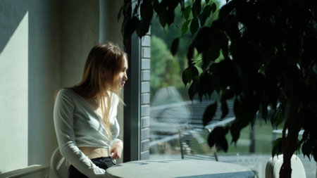 Sad young girl, teenager sitting at a cafe table in the rays of the bright summer sunの写真素材