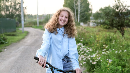 Cute curly teenager girl riding a bike in the countryside on a summer dayの写真素材
