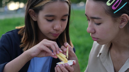 Cute children, two sisters eating French fries outdoors in summer. Unhealthy food for children. Unhealthy food.の写真素材