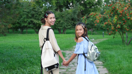 Two girls walking in the park in the summer, talking, walking after school and college, holding hands, best friends, sisters returning home after schoolの写真素材