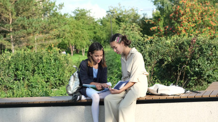 Cute happy little schoolchildren with backpacks and notebooks sitting on a park bench outdoors. Two...