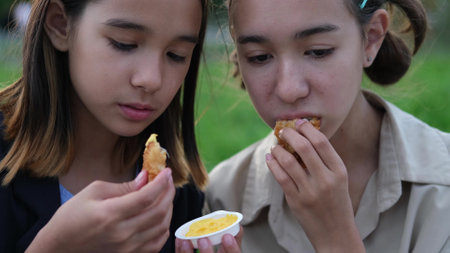Cute children, two sisters eat fast food chicken outdoors in summer. Unhealthy food for children....