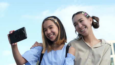 Happy sisters watch a video, take a selfie or talk on a video call using a smartphone outside in the park on a summer day.の写真素材