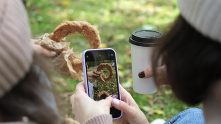 In autumn, two cheerful girls walk through the park during the day, drink coffee and take pictures...