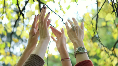 Close-up of two happy womens hands dancing in nature on an autumn day. The womens hands are raised up and move to the music against the backdrop of autumn trees. Religion concept, lifestyleの写真素材