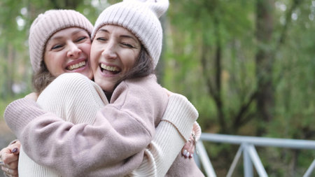 Two women friends or sisters hugging outdoors in autumn park