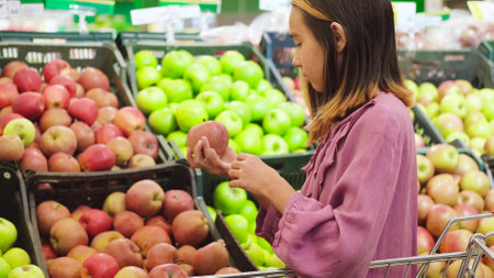 A little girl in a purple dress chooses fruits and vegetables in a grocery store or supermarketの写真素材
