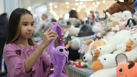 A little girl in a lilac elegant dress against the background of soft toys in a store. A child chooses a toy as a giftの写真素材