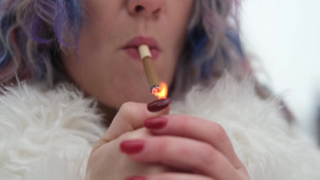 A woman with bright colored hair, wearing a white fur coat, smokes a cigarette outdoors in winter. Young woman in casual urban styleの写真素材