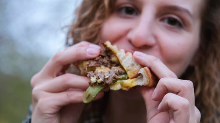 Young woman with curly hair bites and eats an appetizing delicioの写真素材