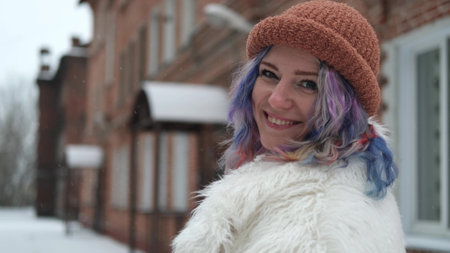 A woman walks on the street on a winter day. A woman with bright multi-colored hair is wearing a white faux fur coat. Theres snow all around herの写真素材