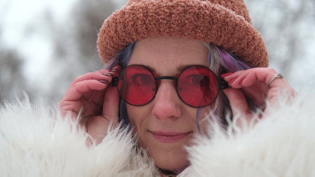 Portrait of a woman in sunglasses and a white fur coat in winter. Woman with colored curly hair posing outdoors during snowfallの写真素材