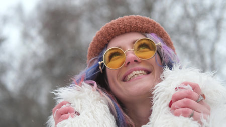 Portrait of a woman in sunglasses and a white fur coat in winter. Woman with colored curly hair posing outdoors during snowfallの写真素材