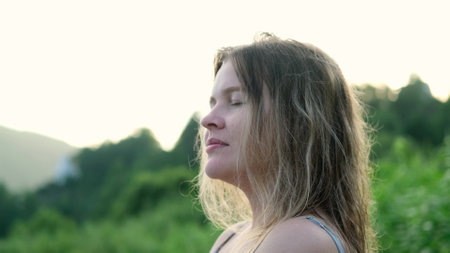 Beautiful young woman relaxing and enjoying the sun at sunset. Profile portrait of a girl against the backdrop of summer nature. Pretty happy lady enjoying summer outdoors. Positive emotions, life success, peace concept.の写真素材