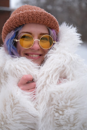 Portrait of a woman in sunglasses and a white fur coat in winter. Woman with colored curly hair posing outdoors during snowfallの写真素材