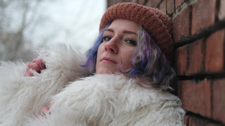 A woman layers near the brick wall of an old house on a winter day. A woman with bright...