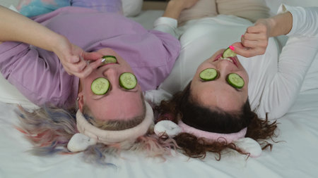 Two girlfriends are relaxing at home in the bedroom and making a face mask. Cheerful rest of two women in pajamas. Cosmetic procedures. Skin care.の写真素材