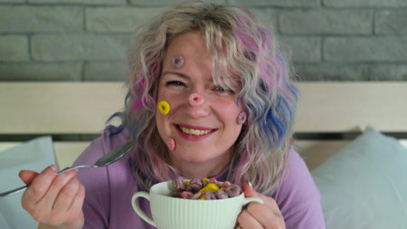 Cute cheerful woman with bright hair eats dry childrens breakfast, multi-colored rings in a white plateの写真素材