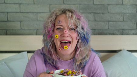 Cute cheerful woman with bright hair eats dry childrens breakfast, multi-colored rings in a white...