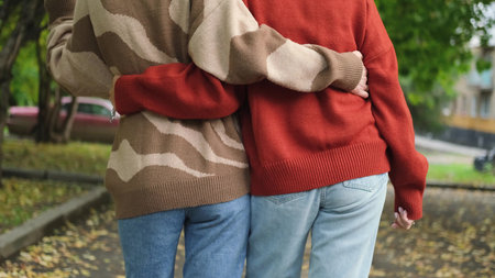 Two girlfriends are walking and having fun outside among autumn trees in a city park.の写真素材