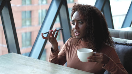 A very beautiful African American woman with long hair listens to a voice message on a smartphone...