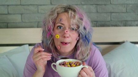 Cute cheerful woman with bright hair eats dry childrens breakfast, multi-colored rings in a white...