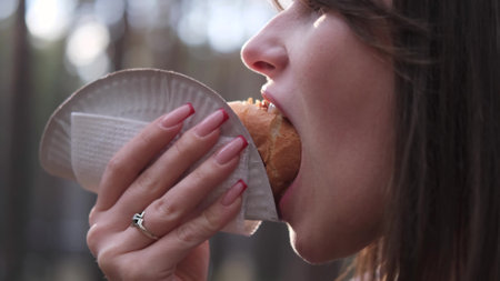 A woman eats a hot dog while walking outdoors in a park or forest. Close-upの写真素材