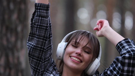 Young beautiful brunette listens to music on headphones outdoors. A woman dances joyfully to music...