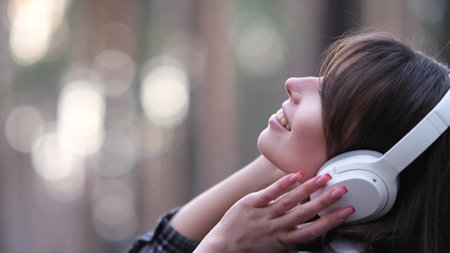 Young beautiful brunette listens to music on headphones outdoors. A woman dances joyfully to music among the maidens in the forest.の写真素材