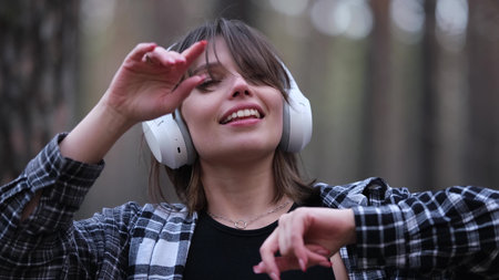Young beautiful brunette listens to music on headphones outdoors. A woman dances joyfully to music...