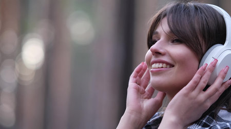Young beautiful brunette listens to music on headphones outdoors. A woman dances joyfully to music among the maidens in the forest.の写真素材