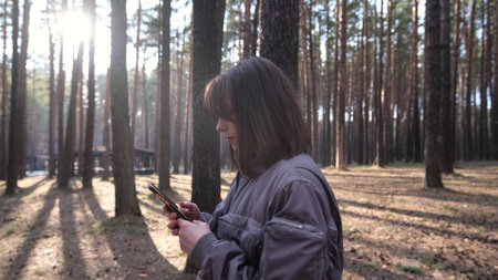 A girl tourist walks through the forest and uses a GPS smartphone, writes a text message on social networks.の写真素材